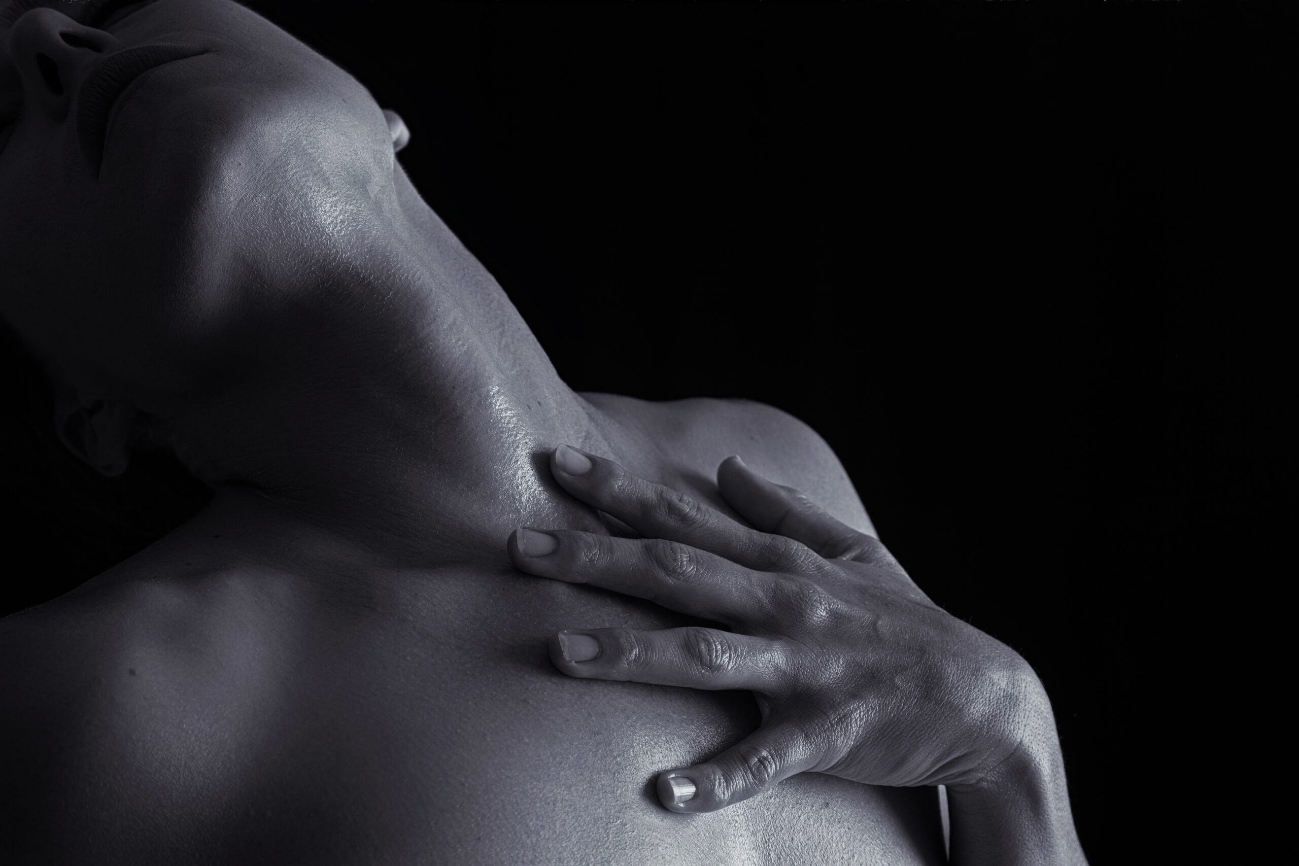 A hand resting on a bare shoulder and neck, softly lit in black and white