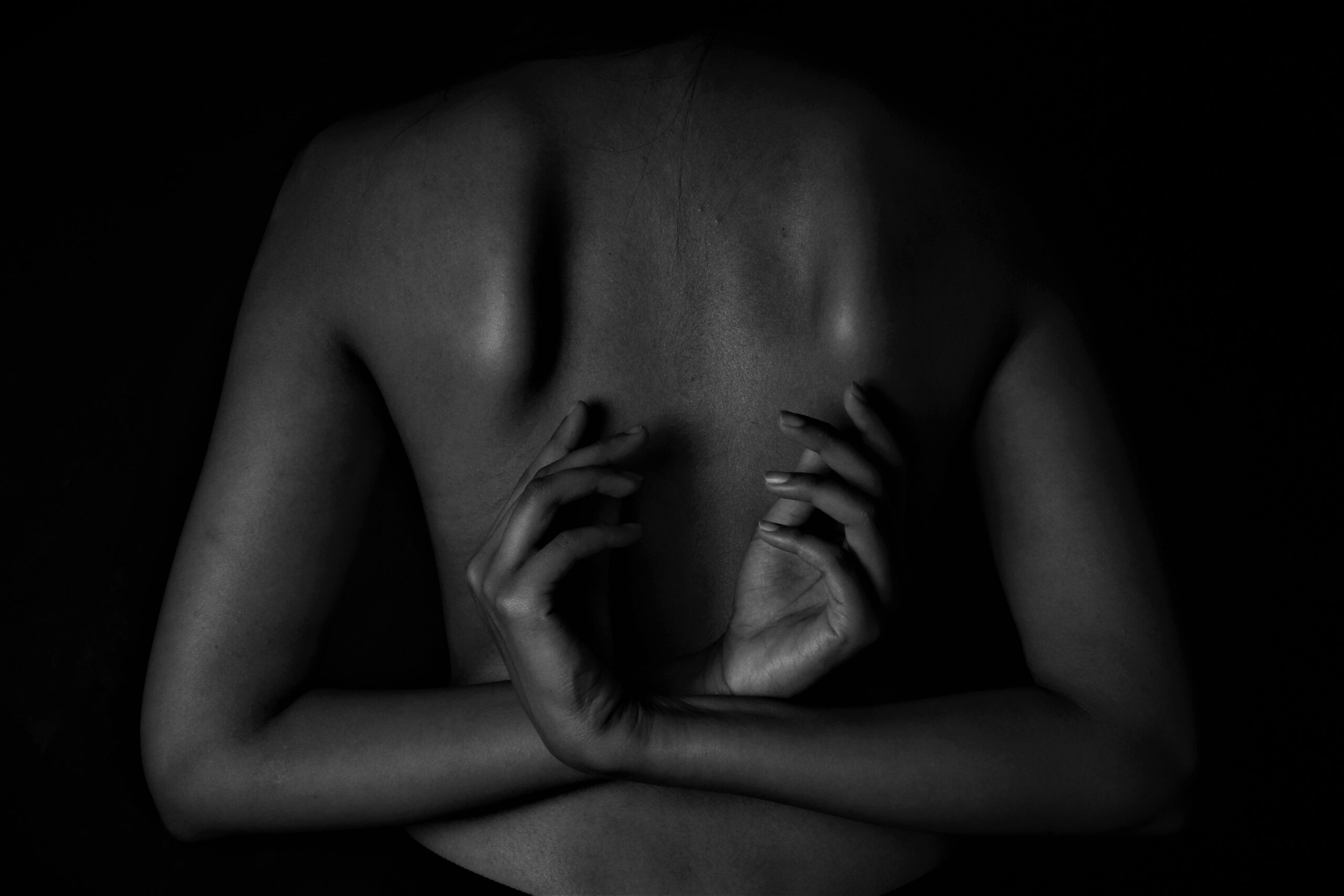 A bare back, arms crossed and hands resting against the shoulder blades in near darkness