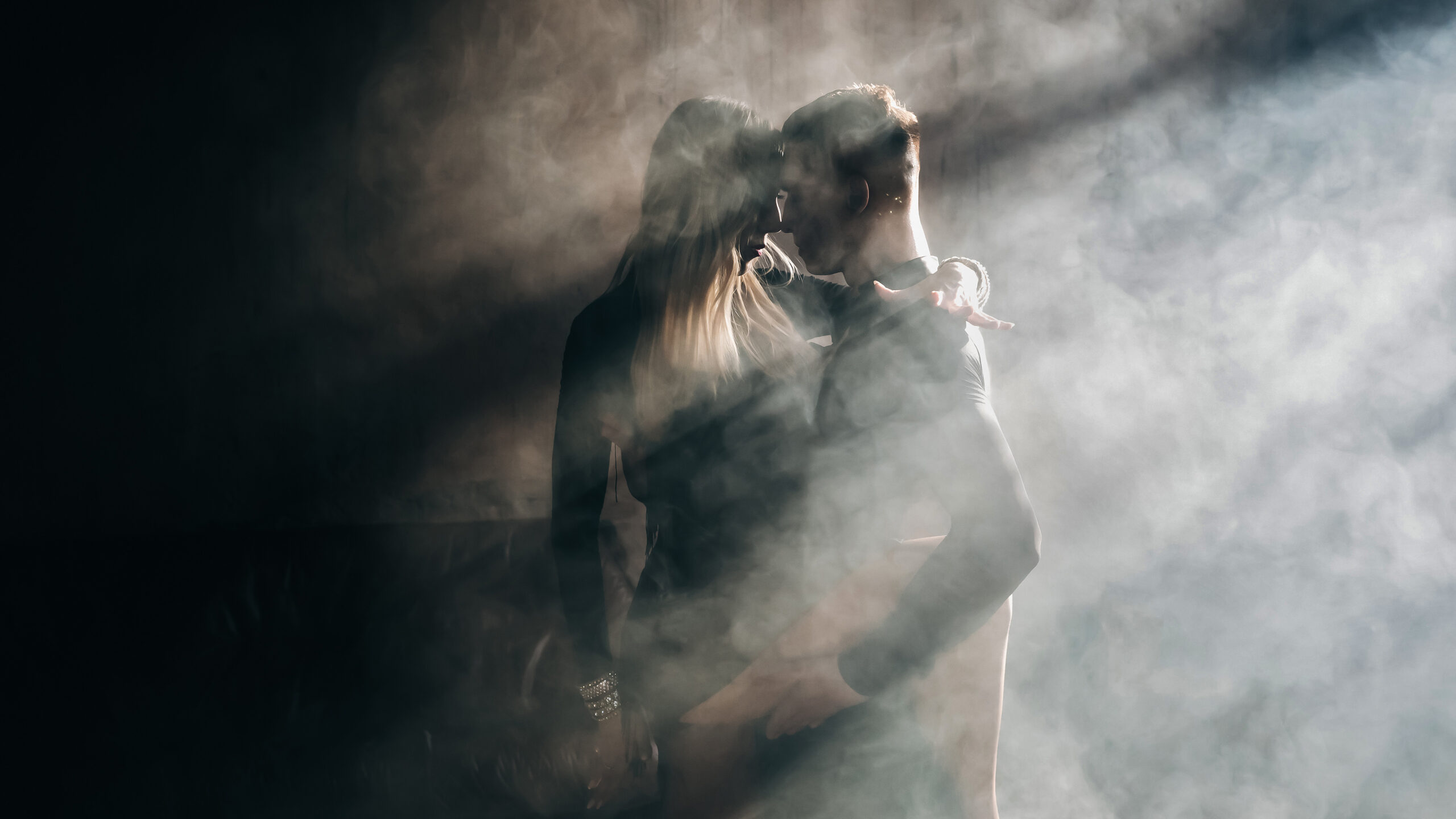 Two figures embracing in shafts of light breaking through drifting smoke